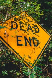 Close-up of a bright yellow dead end sign obscured by leaves, symbolizing caution.