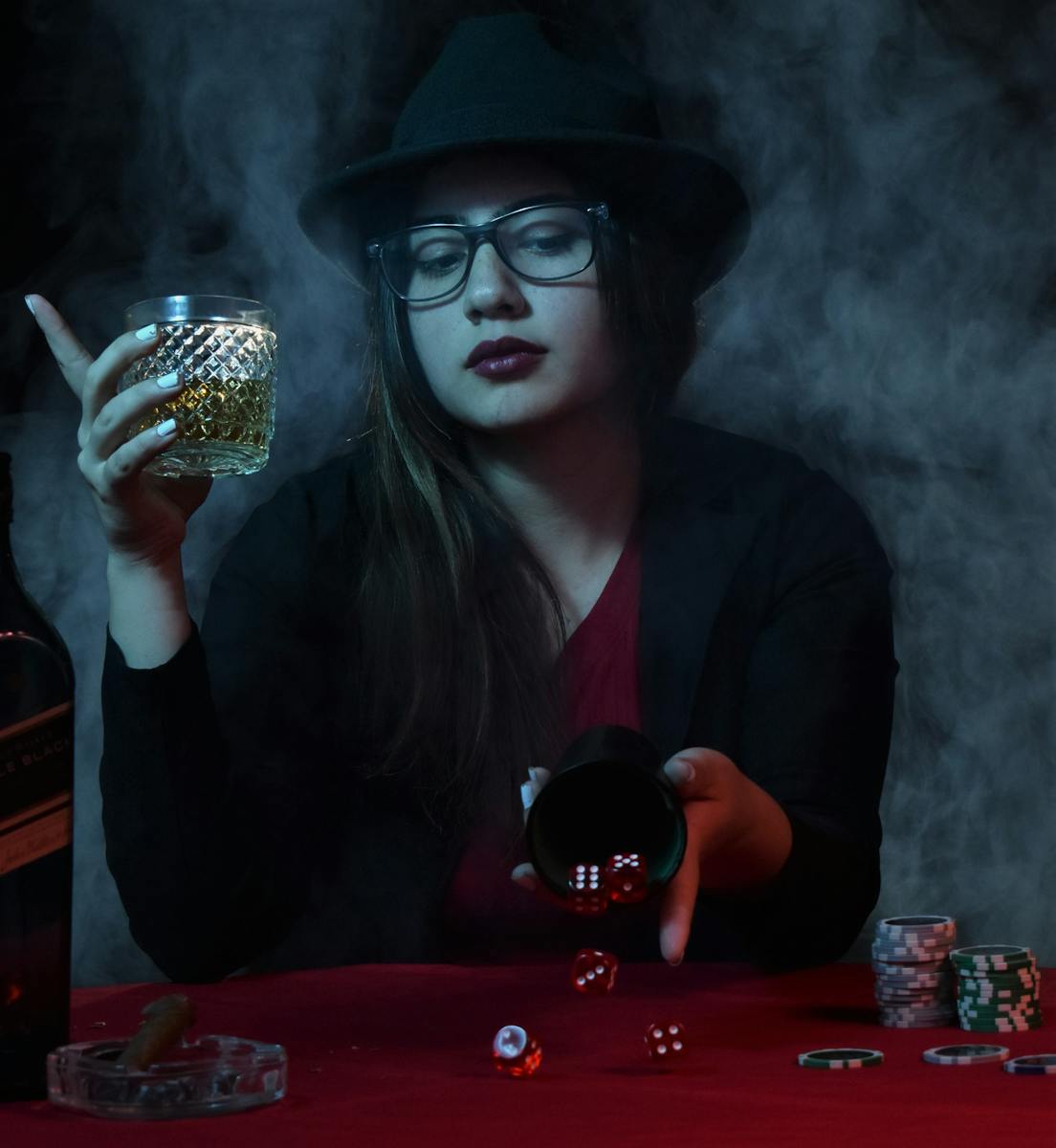 Woman with drink playing dice amidst casino smoke, evoking a mysterious nightlife vibe.