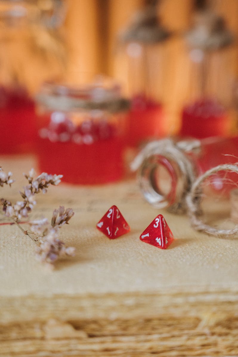 Close-up view of red tetrahedral dice amidst rustic jars and burlap on a natural surface.