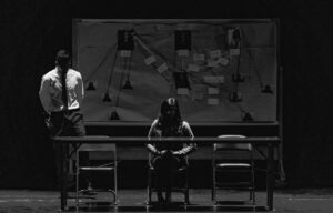 Black and white scene depicting a tense interrogation with suspect and investigator.