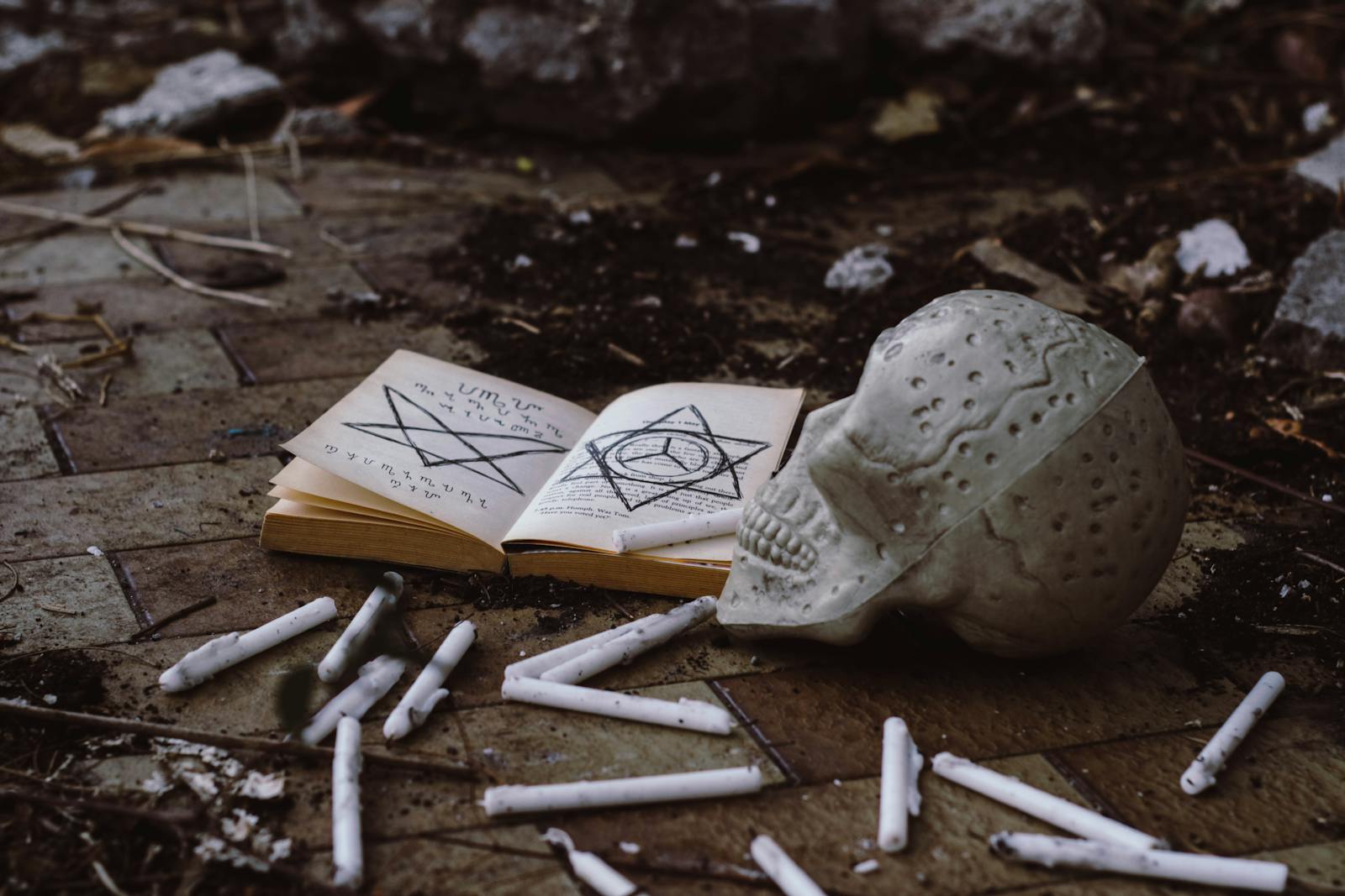 A creepy setup with a spellbook, skull, and candles on the ground, evoking Halloween vibes.