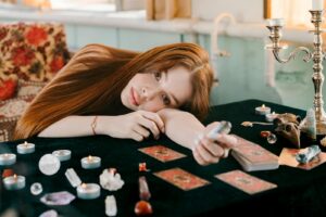 A woman engaged in tarot reading surrounded by candles and crystals on a table.