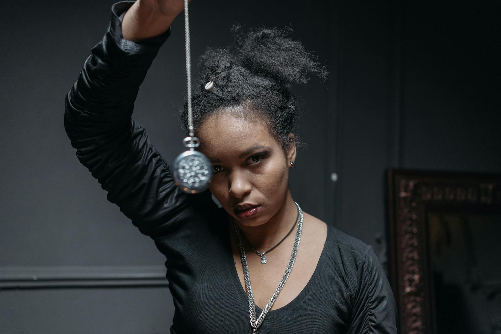 A black woman conducting a spiritual ritual indoors with a pendant, evoking mystical themes.