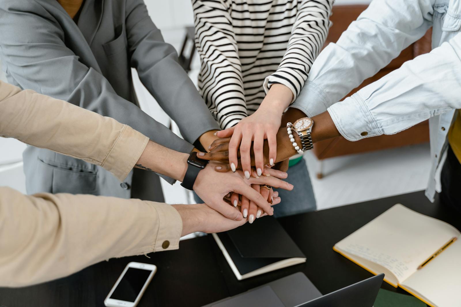 A group of diverse colleagues joins hands in teamwork, symbolizing unity and collaboration.