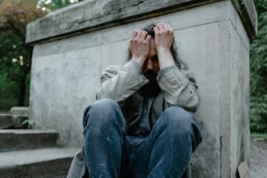 A homeless man sits in distress against a concrete wall, symbolizing poverty and isolation.
