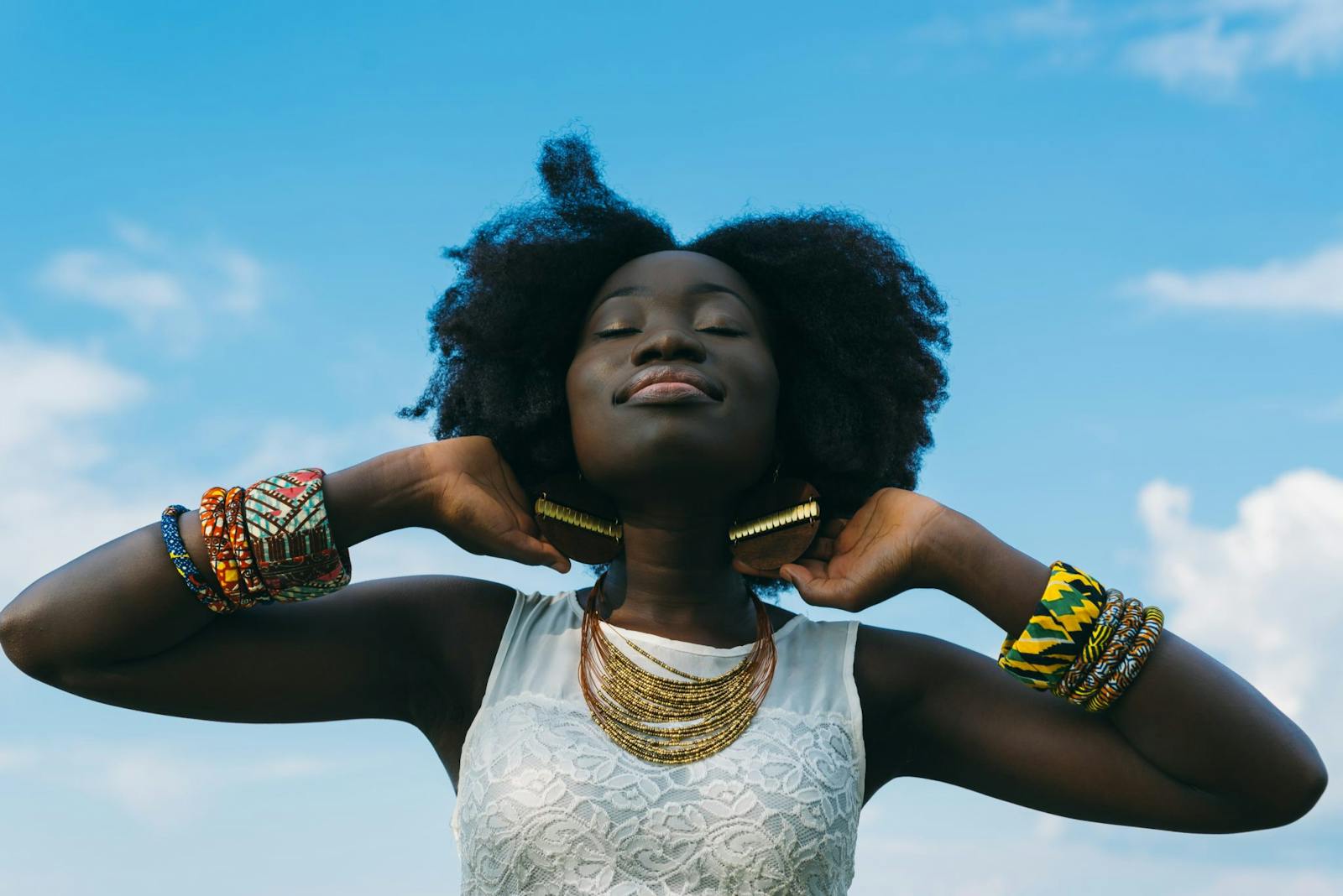 Portrait of a joyful African woman with afro hair, wearing colorful bracelets and gold earrings, enjoying the sunny day.