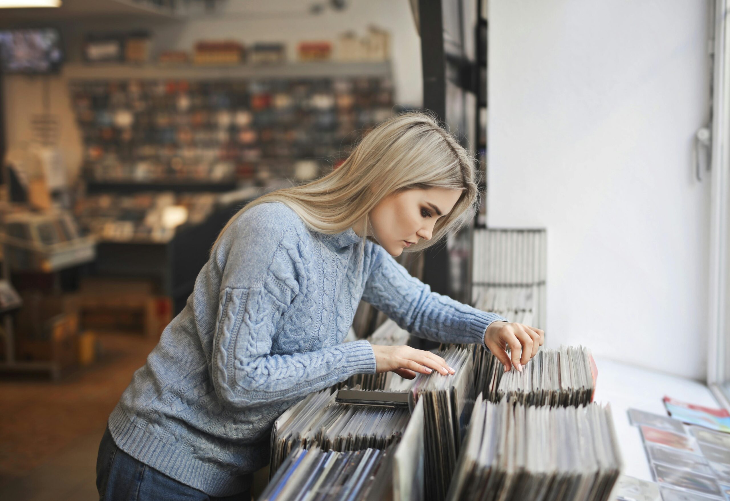 Selective focus side view photo girl in gray sweater selecting vinyl records from a music store