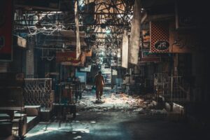 A solitary figure walks through an abandoned urban alley littered with debris, capturing urban decay.