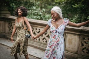 Two women enjoying a walk outdoors, holding hands and smiling in floral dresses.
