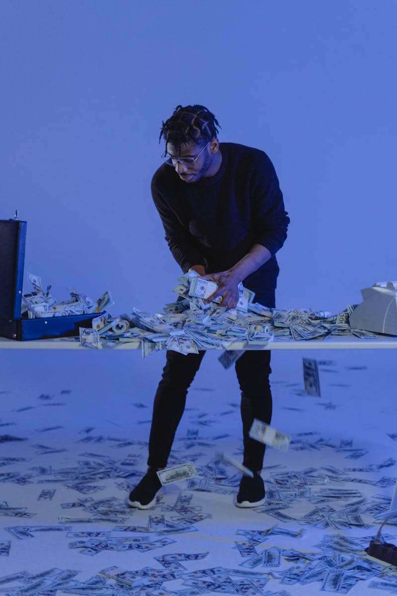 A man interacts with scattered dollar bills in a blue-lit modern setting.