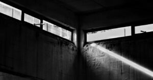 Grayscale photo of windows in an abandoned concrete interior with dramatic light.