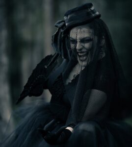 Gothic woman in dark attire with a netted veil and lace umbrella, exuding mystery.